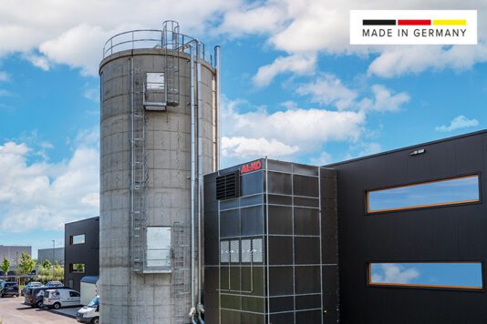AL-KO Absauganlage an einer industriellen Werkhalle mit grauem Filtergehäuse, silbernen Rohrleitungen und Maschinenanschluss