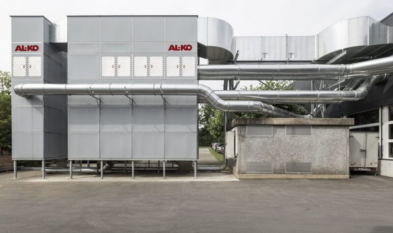 Industrielle AL-KO Absauganlage im Außenbereich mit großer metallischer Filteranlage, mehreren silbernen Rohrleitungen und Anschluss an ein Gebäude