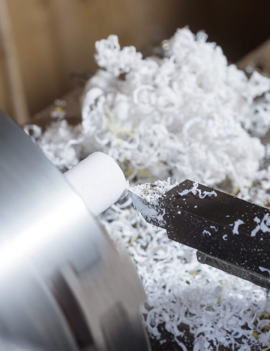 Drehmaschine bei der Bearbeitung eines weißen Werkstücks mit Schneidwerkzeug und vielen hellen Kunststoffspänen